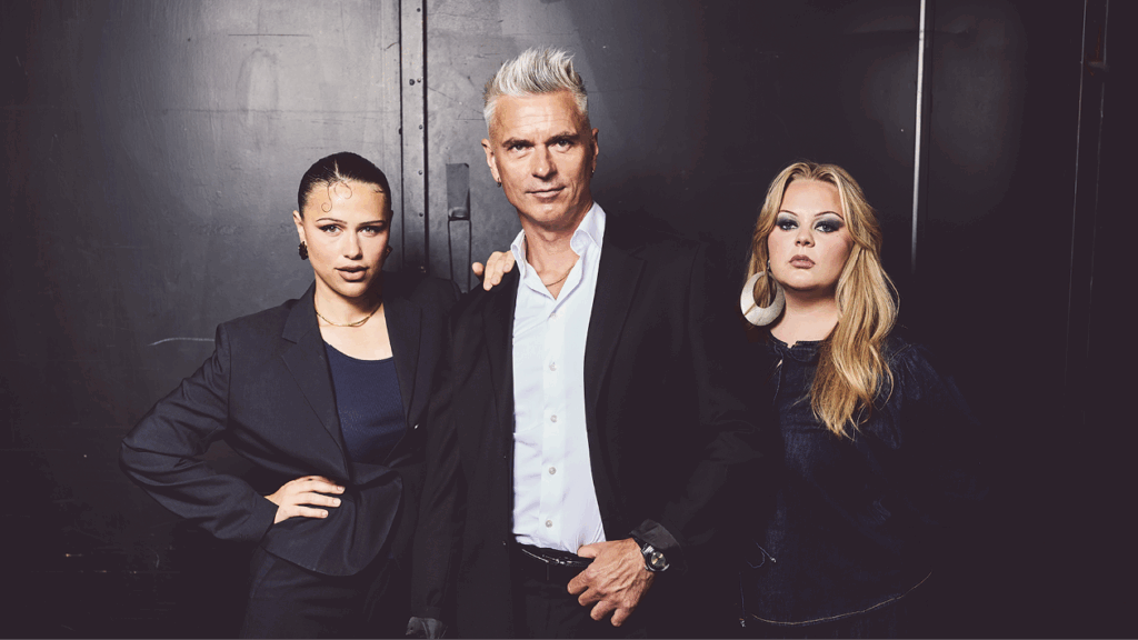 To kvinner og en mann i pyntede klær foran en sort vegg.