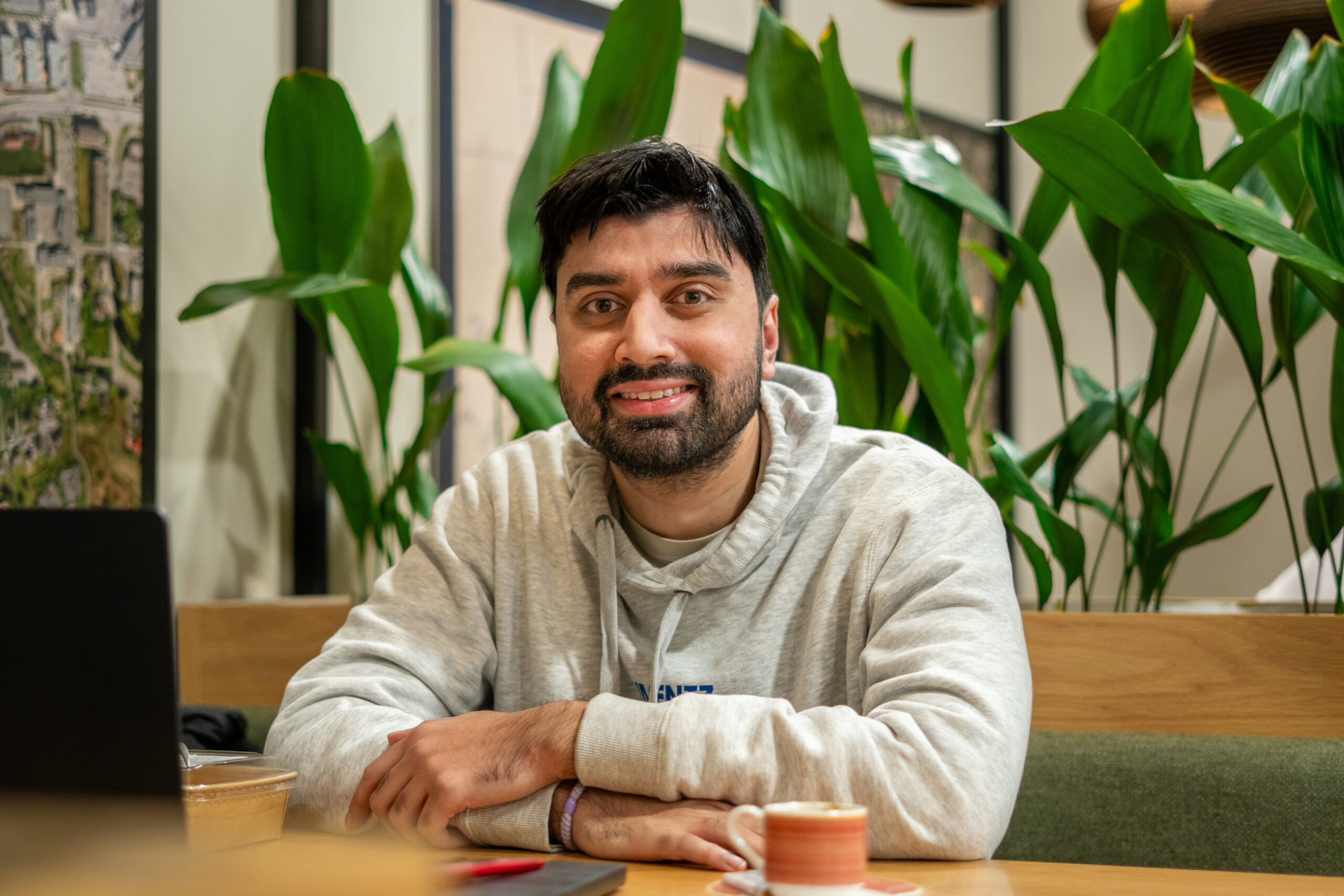 Mann av pakistansk opprinnelse, som sitter i kafémiljø med grønne planter i bakgrunnen.